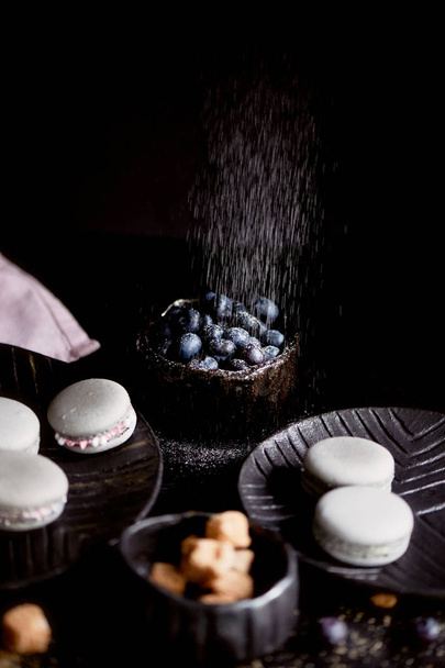 The photo in the dark gray scheme.Grey cake macaron. Macro. Blueberries, which strewed powdered sugar. - Fotó, kép