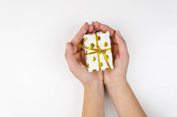 Woman holding small golden present box in hands on a white background.Flatly, top view - Foto, afbeelding