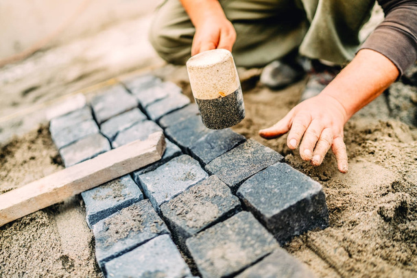 Male construction worker using granite cobblestone blocks to create path or sidewalk - Photo, Image