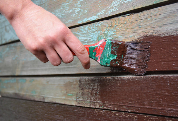 Painting old wooden wall with worker hand. Painting with red brush - Photo, Image