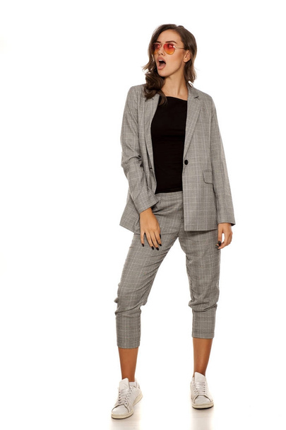 Beautiful woman with sunglasses posing in casual women`s suit and sneakers - Photo, image