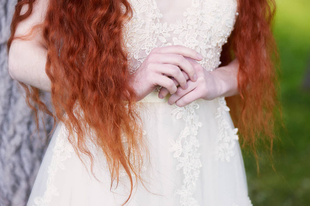 Beautiful red-haired girl with long curly hair in the bride, in a long lace dress.A natural beauty. - Фото, изображение