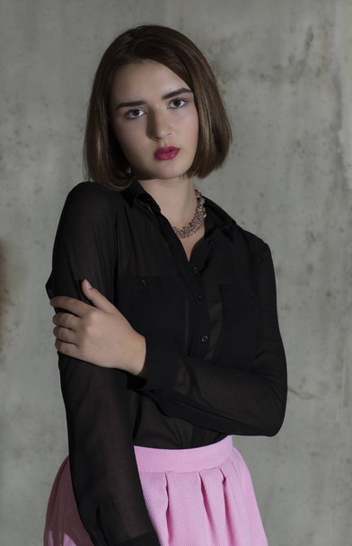 Young woman standing in her black long sleeved shirt and pink skirt - Foto, Bild