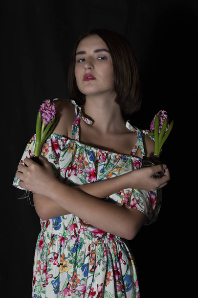Attractive girl holding two fresh wrenched hyacinth flowers by crossed arms. - Фото, изображение