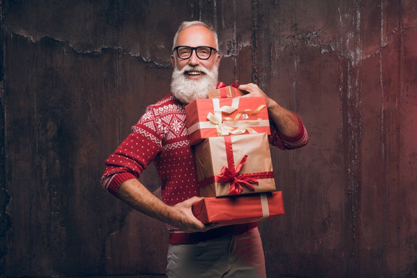 Szép vezető szakállas ember holding díszdobozban, mint sötét háttér és látszó-on fényképezőgép. Santa Claus kíván kellemes karácsonyi ünnepeket és boldog új évet.   - Fotó, kép