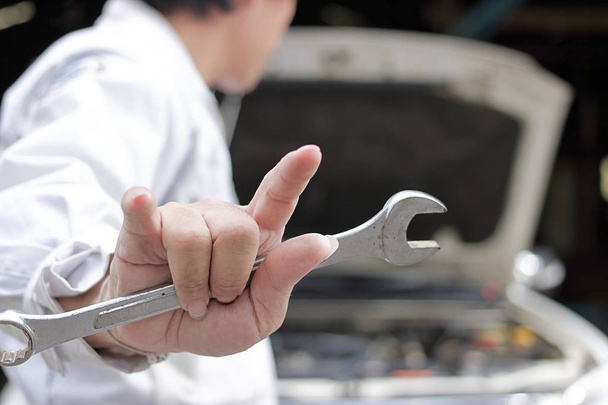 Achteraanzicht van de mechanische mens auto bedrijf moersleutel en zijn hand met ik hou van je bord met auto in open kap op de achtergrond van de garage reparatie. - Foto, afbeelding