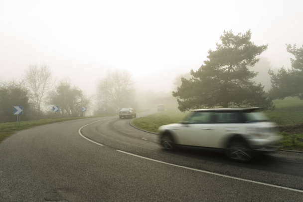 neblig asphaltierte kurvenreiche Straße mit Autos, die durch den Wald fahren. Wetter mit schlechter Sicht in der Region Normandie, Frankreich. Landschaft an einem nebligen Tag. gemildert - Foto, Bild