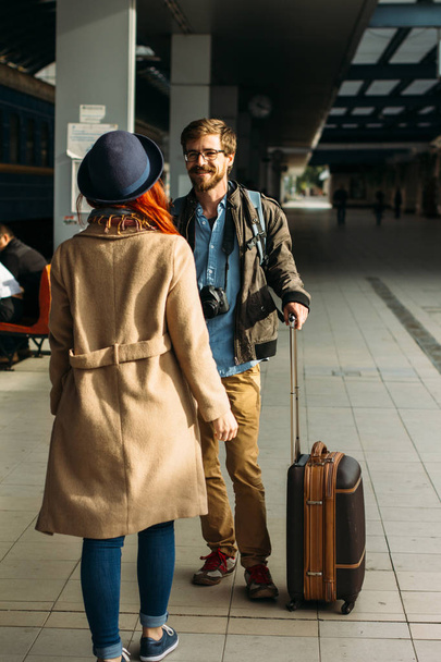Woman meeting her boyfriend from his trip at the train station. Tourist Man with luggage and photo camers. Travel concept. Redhair girlfriend. - Φωτογραφία, εικόνα