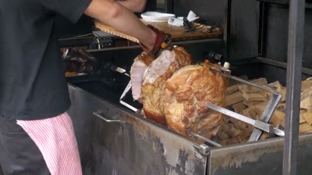 Large Piece meat Roast Pork Leg prepared on a Spit above an Open Fire. Street food in Prague, Czech Republic. - Materiał filmowy, wideo