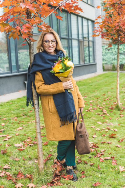 stijlvolle vrouw met bloemen in de herfst park - Foto, afbeelding