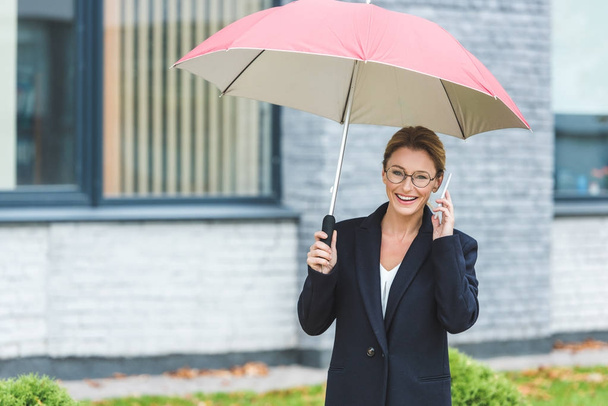 mature woman with umbrella and smartphone - Φωτογραφία, εικόνα