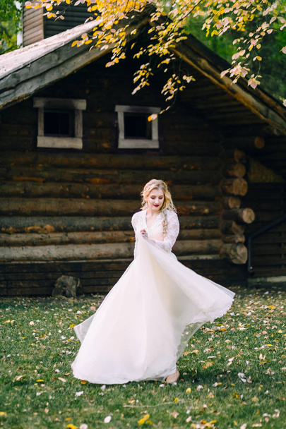 The Beautiful bride is spinning around herself in fluttering dress on wooden house background. Artwork - Foto, Imagen