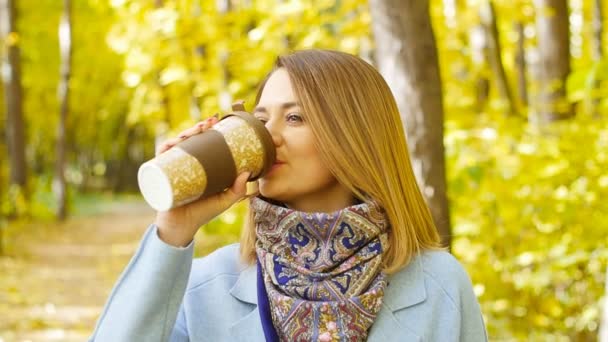 Cute young woman with cup of coffee in the autumn park - Video, Çekim