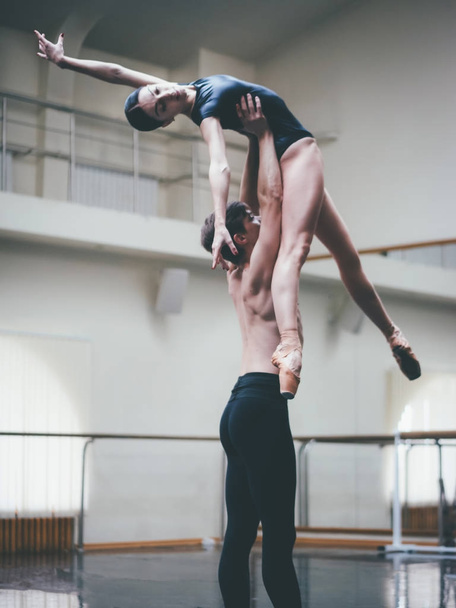 Young man practicing in classical ballet with young beautiful woman in black clothing in the gym or ballet hall. Couple jumping dancing sensual dance. Minimalism interior, - Фото, изображение