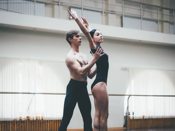 Young man practicing in classical ballet with young beautiful woman in black clothing in the gym or ballet hall. Couple jumping dancing sensual dance. Minimalism interior, - Foto, Imagem