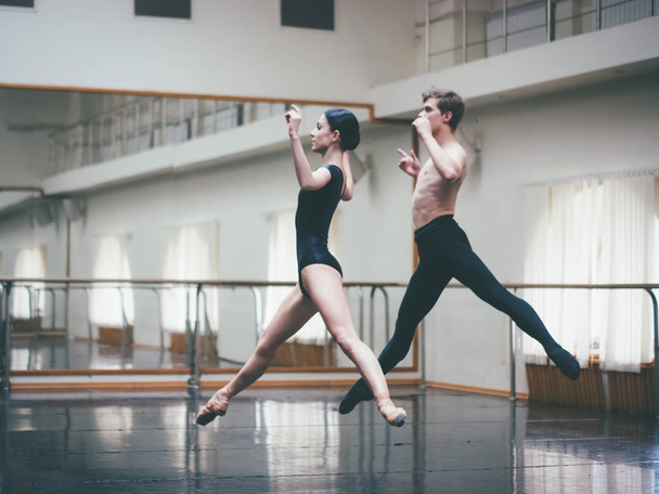 Young man practicing in classical ballet with young beautiful woman in black clothing in the gym or ballet hall. Couple jumping dancing sensual dance. Minimalism interior, - Foto, immagini