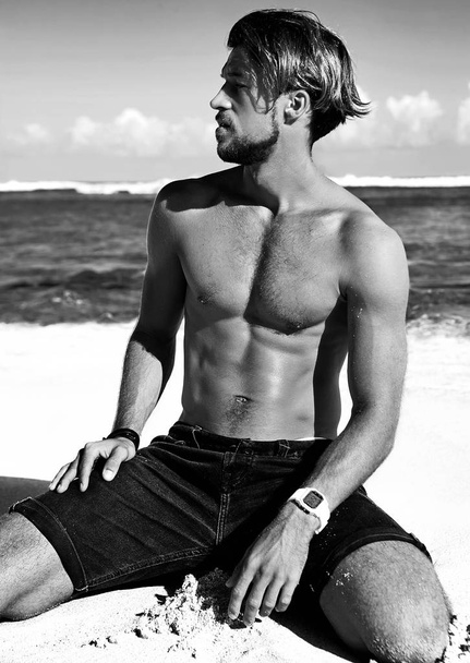 Portrait of handsome sunbathed fashion man model posing on summer beach with white sand on blue sky and ocean background - Φωτογραφία, εικόνα