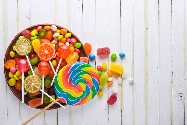 Colored candies, sweets and lollipops. On a white wooden background. Top view. Free space. - Φωτογραφία, εικόνα