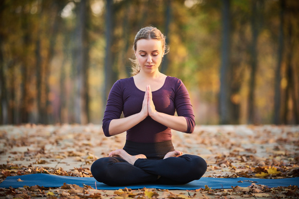 Hermosa joven medita en yoga asana Padmasana - pose de loto en la cubierta de madera en el parque de otoño
. - Foto, Imagen