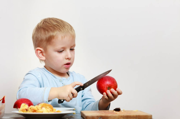 Little boy peeling apples with knife and eating - Фото, зображення