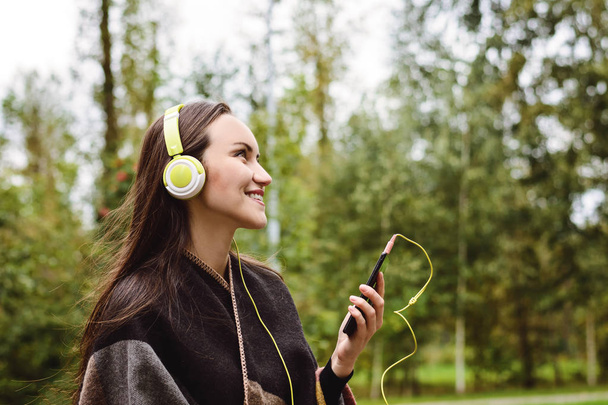 Fiatal, boldog asszony hallgat zenét a smartphone-val a fejhallgató, egy csendes parkban - Fotó, kép
