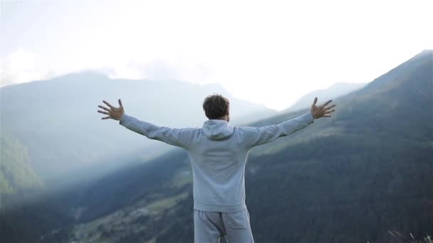 Man raises hands up standing back on mountain top morning sun shine slow motion. No face male silhouette figure in sportswear enjoying life above world. Achievement success motivation winner concept - Footage, Video