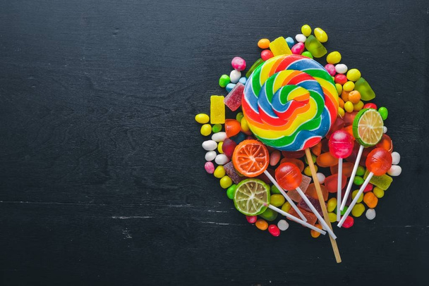 Colored candies, sweets and lollipops. On a black wooden background. Top view. Free space. - Φωτογραφία, εικόνα