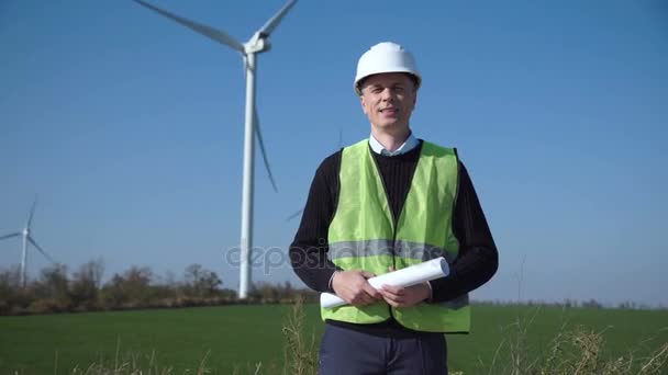 Uśmiechający się inżynier stojące przed farmy wiatrowej - Materiał filmowy, wideo
