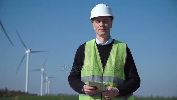 Uśmiechający się inżynier stojące przed farmy wiatrowej - Materiał filmowy, wideo
