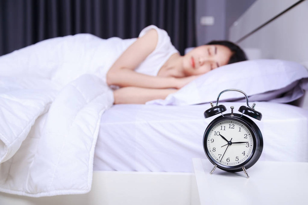 alarm clock on table and woman sleeping on bed in bedroom - Foto, imagen