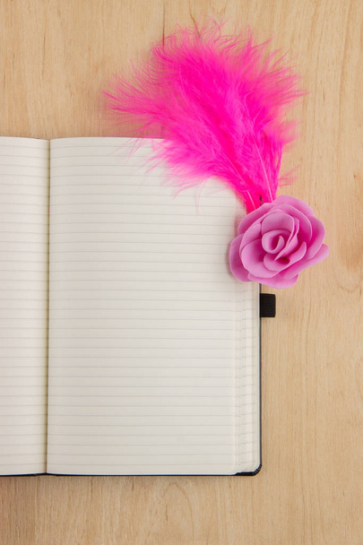 Caderno aberto com páginas brancas e penas rosa em uma aba de madeira
 - Foto, Imagem