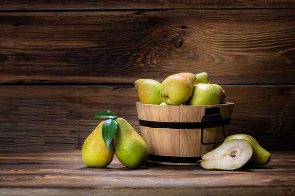 fresh pears with leaves in a basket on wooden background - Foto, afbeelding