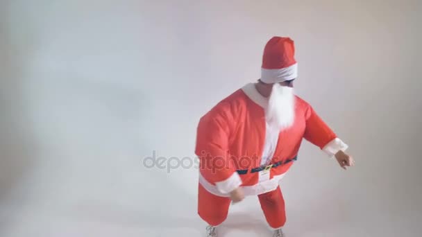 A man in an inflatable Santa costume dances in a white room. - Video