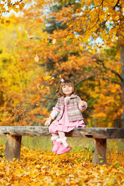 Happy little baby girl sitting on a bench laughing and playing with leaves. In nature, walk in the open air - Fotoğraf, Görsel