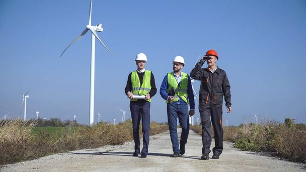 Drie monteurs lopen tegen windmolenpark - Foto, afbeelding