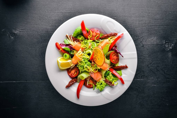Salad with salmon and fresh vegetables and herbs. Italian cuisine. Top view. On Wooden background. - Fotó, kép