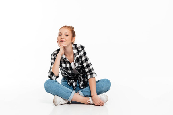 Smiling ginger woman in shirt and jeans sitting on floor - 写真・画像