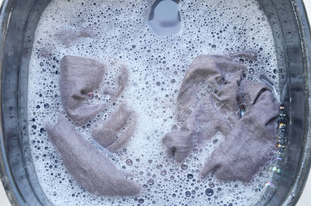  grijs overhemd weken in poeder wasmiddel water ontbinding op zwarte kunststof bekken - Foto, afbeelding