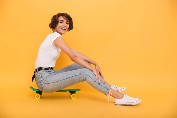 Portrait of a smiling cheerful girl sitting on a skateboard - Photo, image