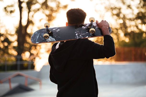 Back view of a male teenager guy holding skateboard - Foto, Imagen
