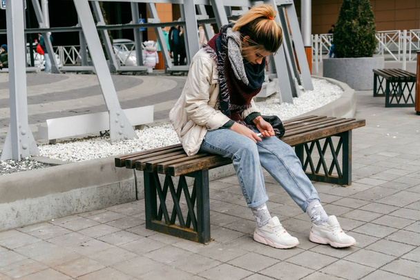 stylish fashionable girl sits on a wooden bench, looks down, looks sad - Photo, Image