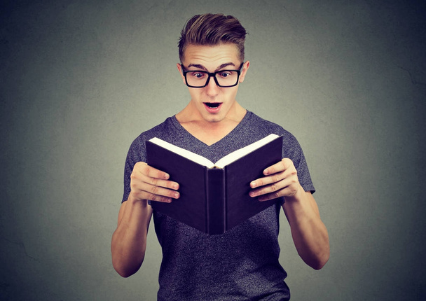 Surprised young man in glasses reading a book - Φωτογραφία, εικόνα