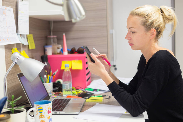 Жінка-підприємець смс на мобільному телефоні в барвистому сучасному творчому робочому середовищі
. - Фото, зображення