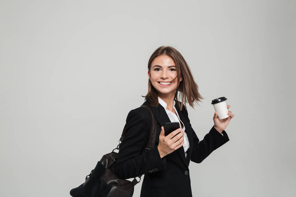 Portrait of a satisfied woman in suit holding mobile phone - 写真・画像