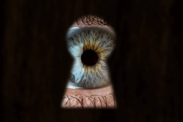 weibliches blaues Auge, das durch das Schlüsselloch schaut. Konzept von Voyeurismus, Neugier, Stalker, Überwachung und Sicherheit - Foto, Bild