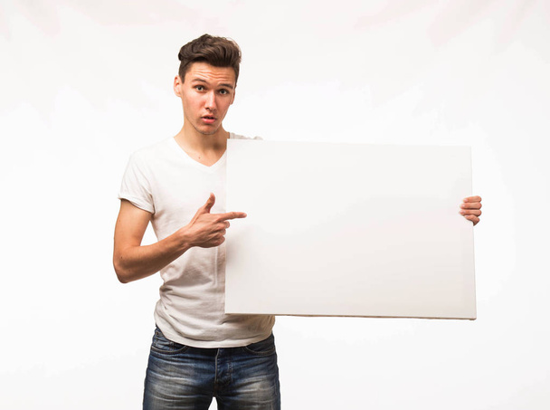 Young surprised man showing presentation, pointing on placard. - Foto, afbeelding
