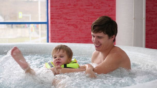 Nuori isä, jolla on lapsi, ui kylpyläaltaassa. Rentoutuminen ja hauskaa altaassa
 - Valokuva, kuva