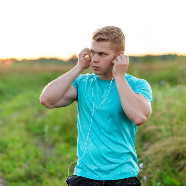 A man atlen stands in the park dresses the headphones, confident look. Summer lifestyle, motivation is strong. Cardigan with a T-shirt. - Фото, изображение