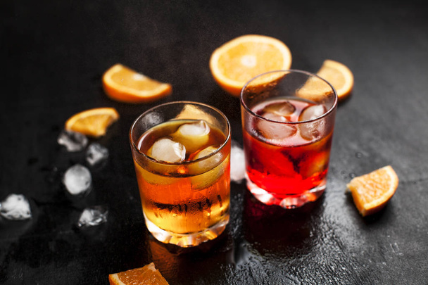 dos vasos con cócteles con hielo con naranja sobre un fondo húmedo oscuro
 - Foto, imagen