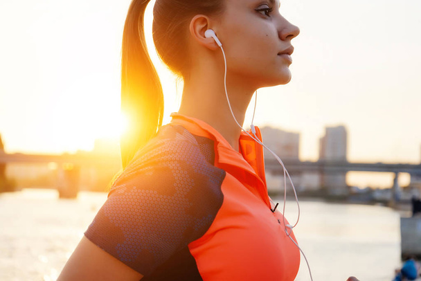 beautiful sports girl engaged in fitness at the river, at sunset, listening to music on headphones - Foto, Imagen